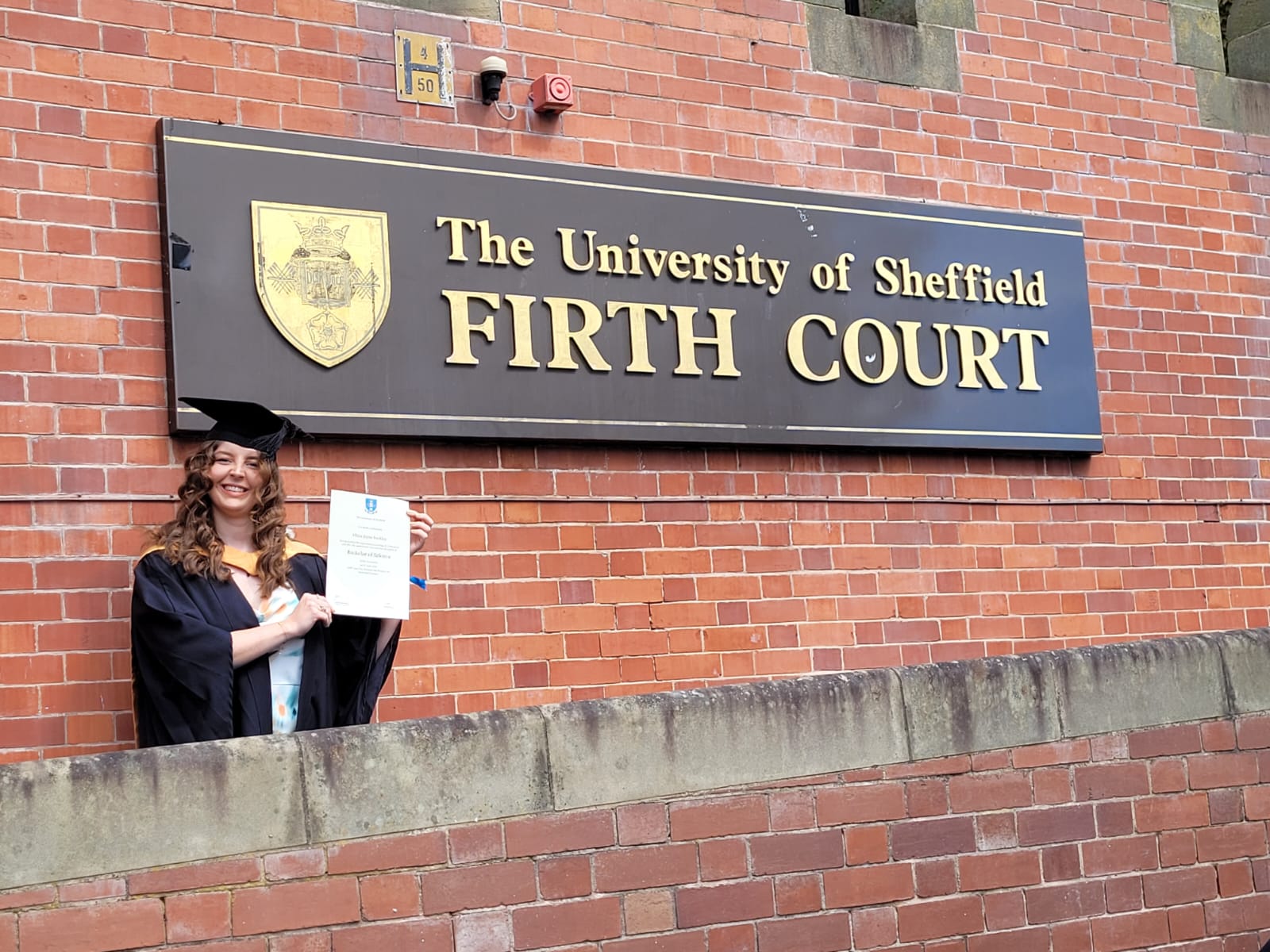 Liv holding up her Biomedical Science Graduation certificate outside Firth Court, at the University of Sheffield.