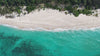 A video of turquoise sea crashing onto white sandy beach with green trees at the back of the beach.